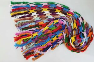 Detalhe de trabalho manual em crochê: Cachecol de crochê com pontos alto e baixo, feito com fio de algodão colorido em formato retangular, destacando tons vibrantes e franjas nas extremidades. — Produzido por Samuel Ramos - Blog do Crochê.