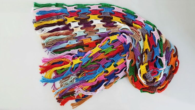 Detalhe de trabalho manual em crochê: Cachecol de crochê com pontos alto e baixo, feito com fio de algodão colorido em formato retangular, destacando tons vibrantes e franjas nas extremidades. — Produzido por Samuel Ramos - Blog do Crochê.