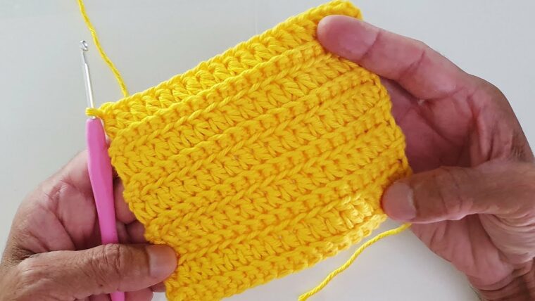 Detalhe de trabalho manual em crochê: Amostra em crochê de ponto alto e relevo, fio de algodão amarelo, formato quadrado, sendo trabalhada com agulha rosa, ideal para tapetes ou mantas decorativas. — Produzido por Samuel Ramos - Blog do Crochê.