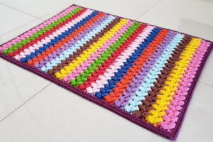 Detalhe de trabalho manual em crochê: Tapete retangular de crochê com ponto pipoca, feito com fio de algodão colorido; tons predominantes: rosa, amarelo, azul, verde, lilás, vermelho e marrom. — Produzido por Samuel Ramos - Blog do Crochê.