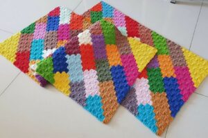 Detalhe de trabalho manual em crochê: Tapete retangular em crochê com ponto pipoca, feito de barbante colorido em tons vibrantes como amarelo, vermelho, azul, verde, rosa e laranja. — Produzido por Samuel Ramos - Blog do Crochê.