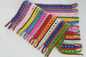 Detalhe de trabalho manual em crochê: Pulseiras de crochê coloridas, feitas com fio de algodão, pontos altos e correntinhas formando faixas retangulares, predominam azul, verde, laranja, vermelho e rosa. — Produzido por Samuel Ramos - Blog do Crochê.