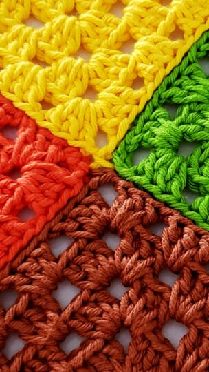 Close-up das mãos do artesão Samuel Ramos realizando uma emenda perfeita em quadradinhos de crochê coloridos usando fio 100% algodão.